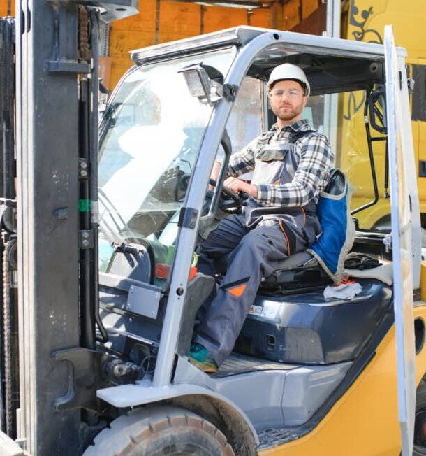 forklift driver in protective vest and forklift standing at warehouse of freight forwarding company